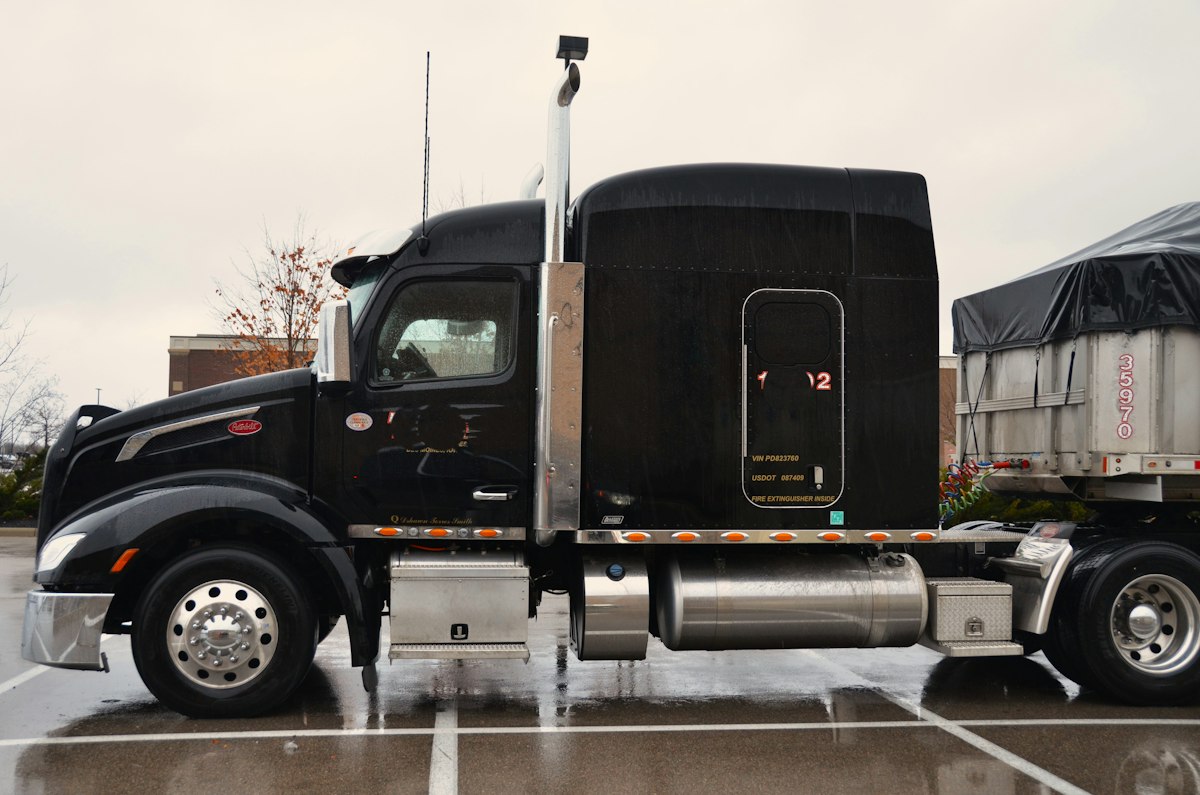 Black sleeper semi-truck with a covered trailer parked in a wet paved lot.